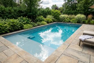 Piscine coque polyester avec plage immergée intégrée dans un jardin aménagé avec dallage en pierre naturelle